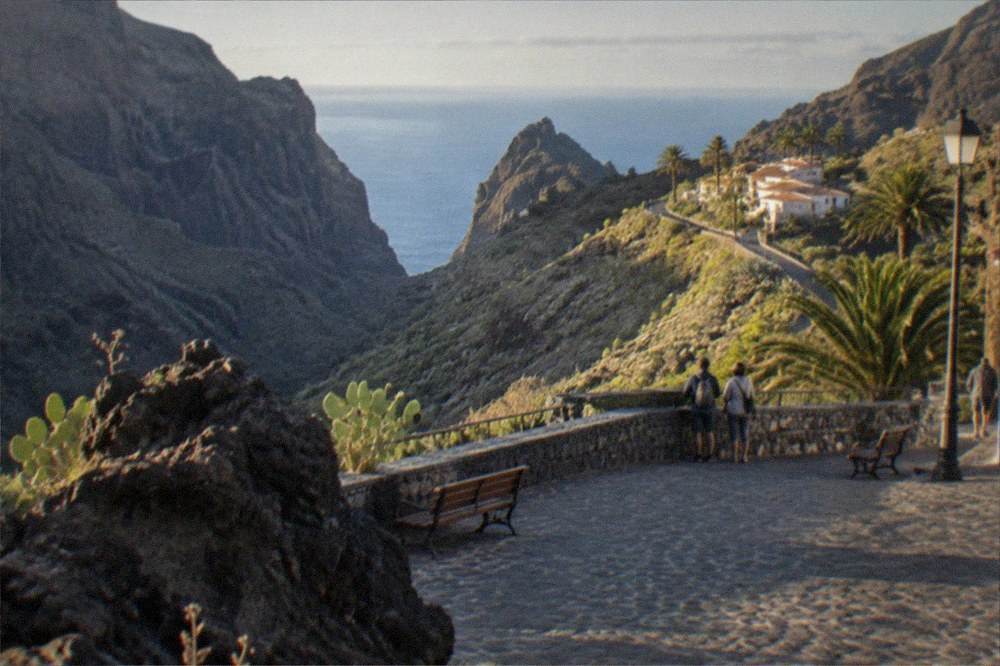 A stone seafront square beside dark lava rock formations along a small coastal town