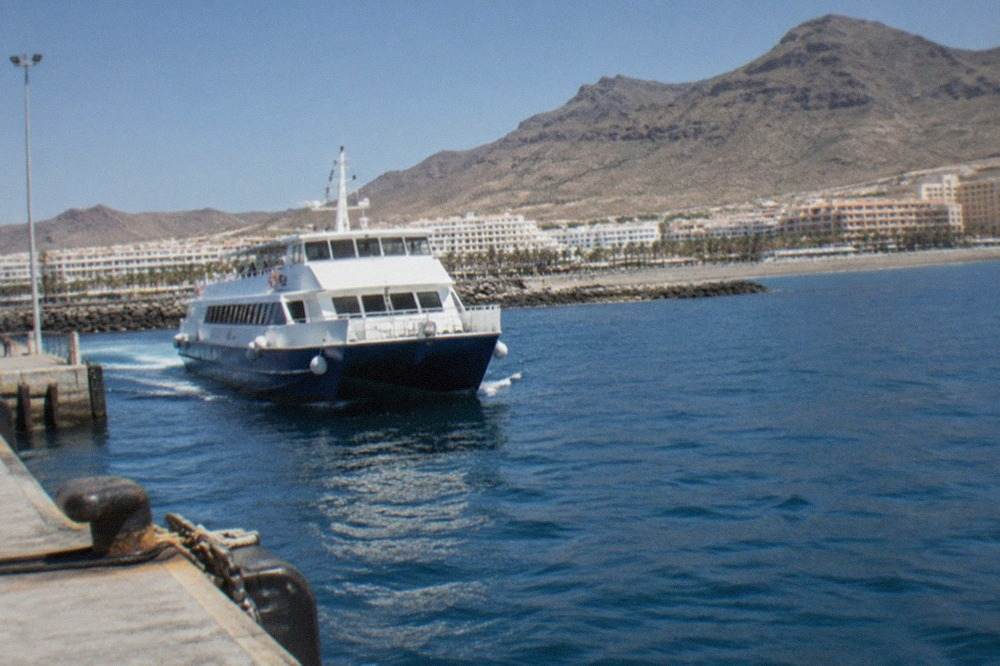 A ferry at the port of Los Cristianos with the Tenerife coastline behind it