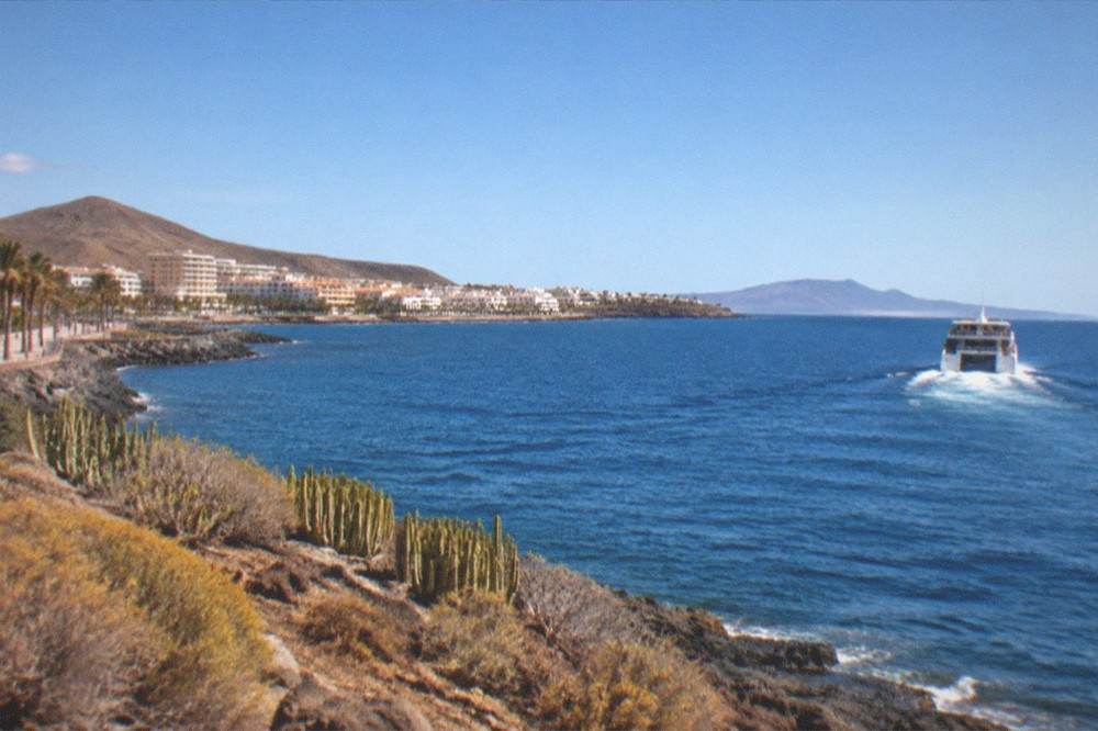A ferry sailing away from Los Cristianos towards a neighbouring island at midday