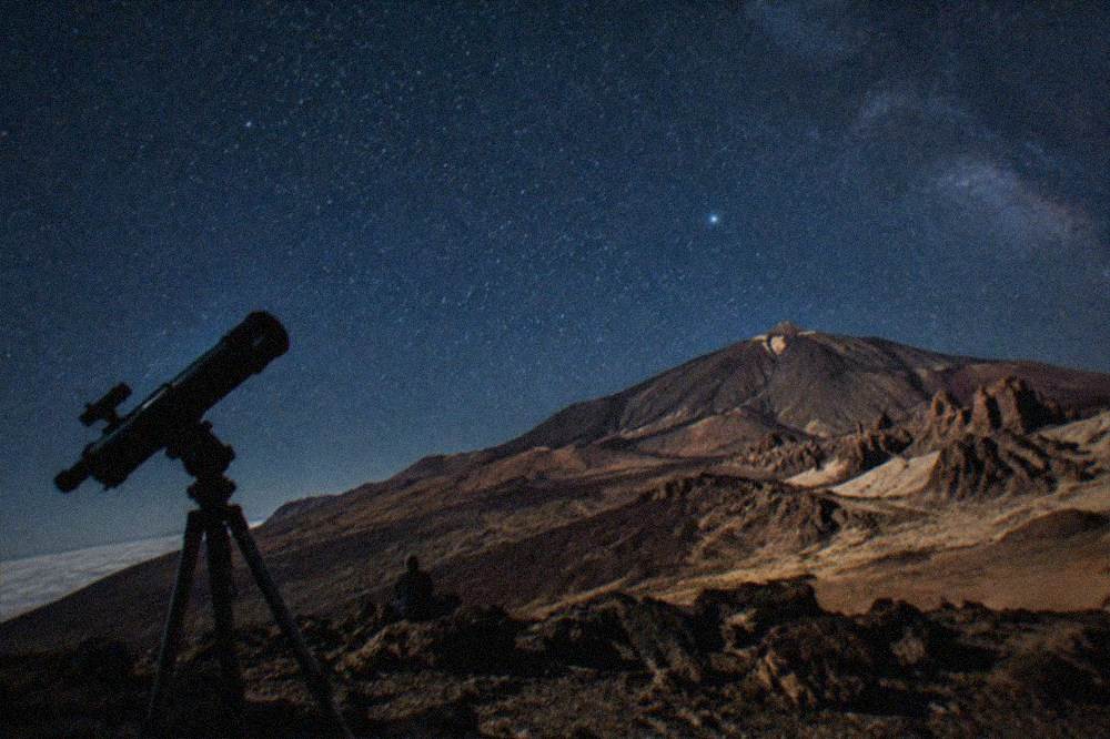 A telescope silhouette against a starry sky above Teide National Park