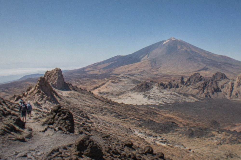 Mount Teide volcano rising above a landscape of dark lava rock under a clear blue sky