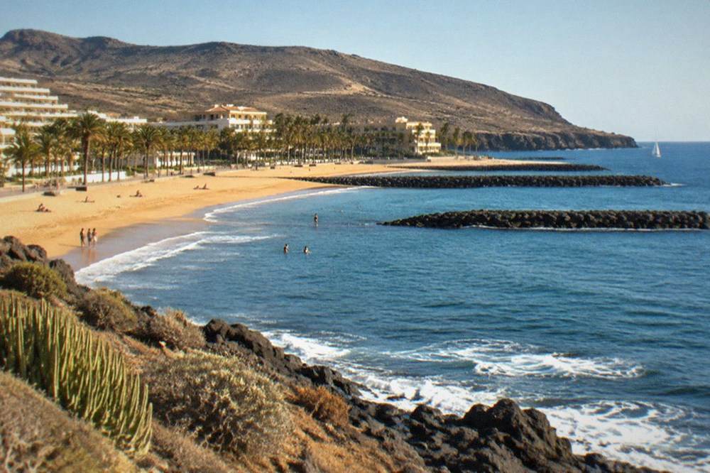 A sheltered Tenerife beach with breakwaters and a smooth promenade behind the sand