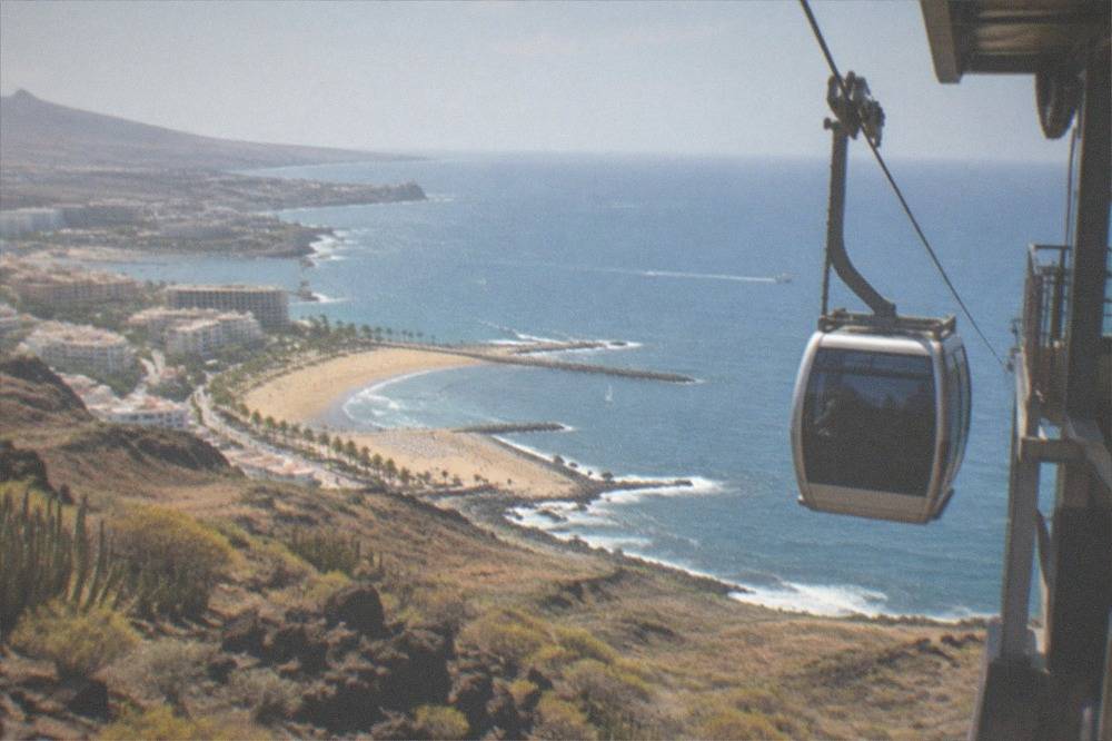 A modern cable car cabin arriving at a high mountain station above volcanic rock