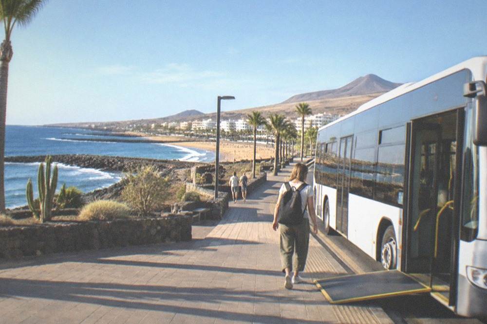 A low-floor public bus at a Tenerife airport stop with a boarding ramp at the door