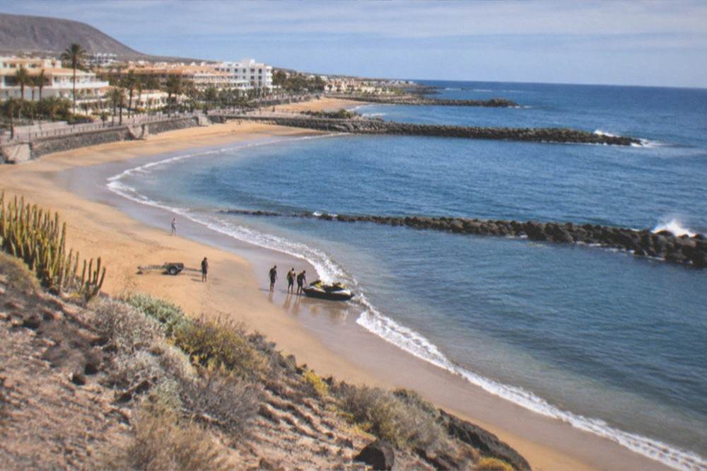A jet ski sitting on a southern Tenerife beach beside calm water with a support crew nearby