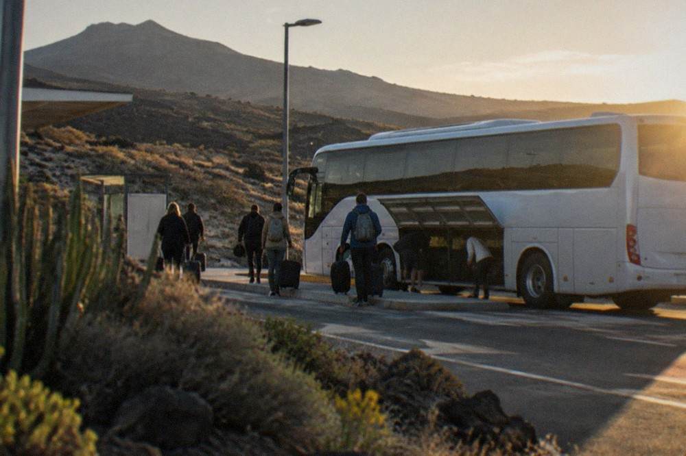 An island bus parked at an airport bus stop with passengers loading luggage into the hold