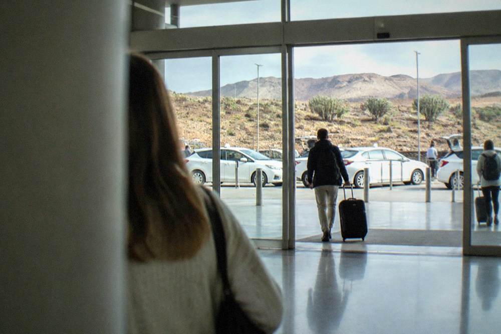 An arrivals hall at a Canary Islands airport with a row of white taxis visible through the glass doors