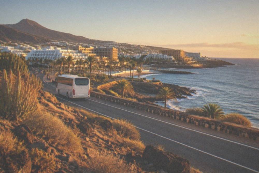 A coastal road through Costa Adeje with resort hotels along the shoreline and a bus in the near distance