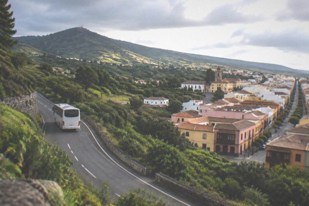 A green hillsided landscape on the plateau around La Laguna, a bus winding along the road