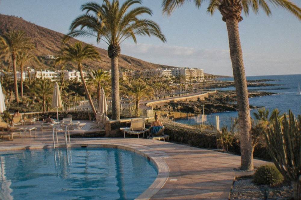 A hotel swimming pool terrace with sun loungers and palm trees under a blue sky in south Tenerife