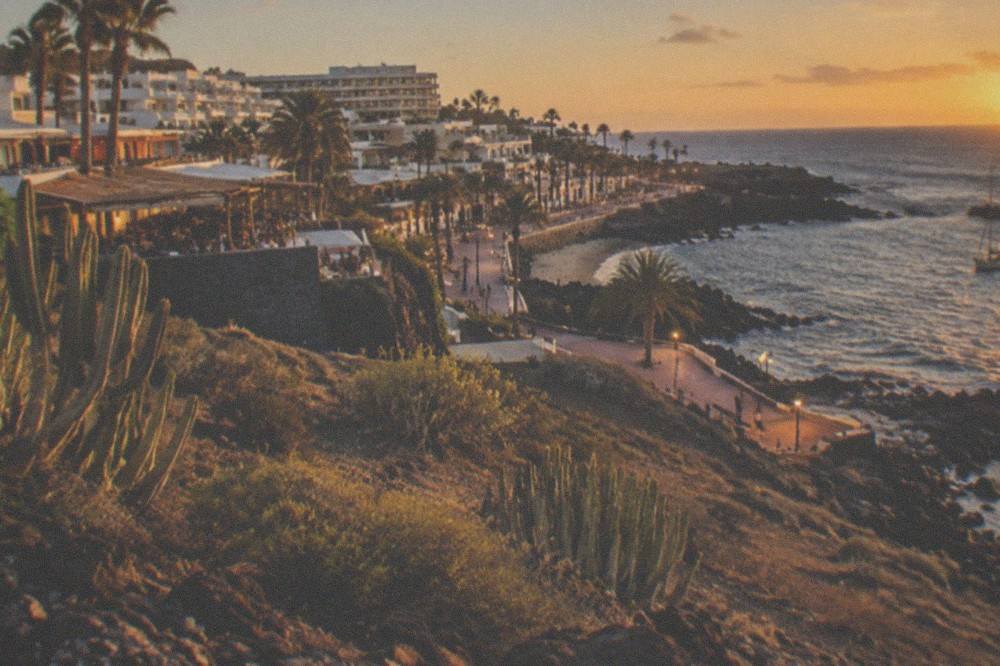 An evening view of a resort town with lit terraces and the sea beyond