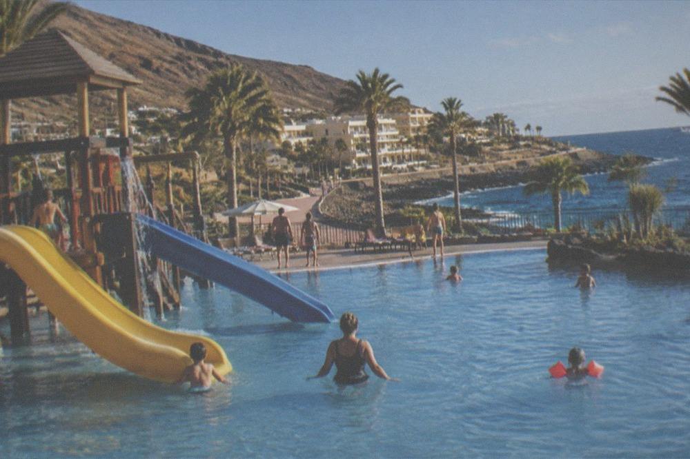 Families with children playing in a resort swimming pool with slides
