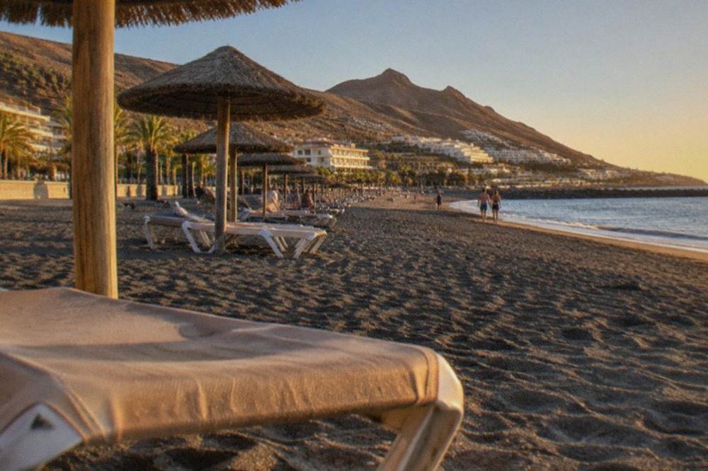 Sunbeds and parasols on a grey sandy beach in Costa Adeje under a clear sky