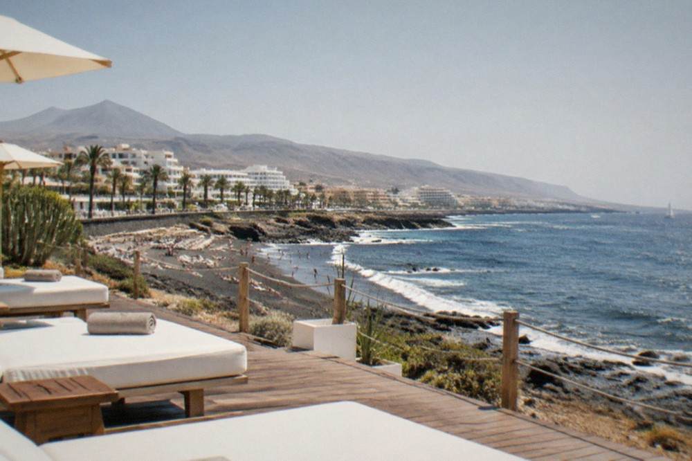 A beach club terrace with white sunbeds, wooden decking and the sea beyond