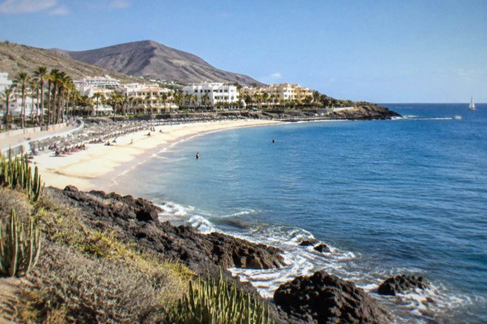 A pale sandy beach with calm water and parasols in Fanabe