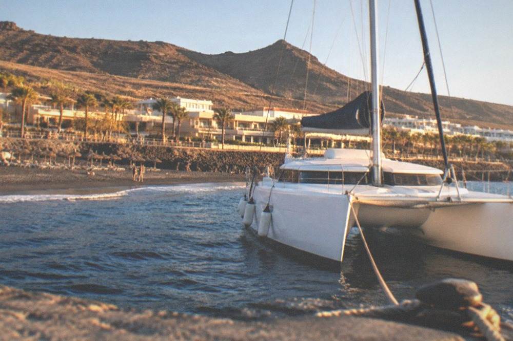 A catamaran moored near a beach club jetty with parasols on the shore behind
