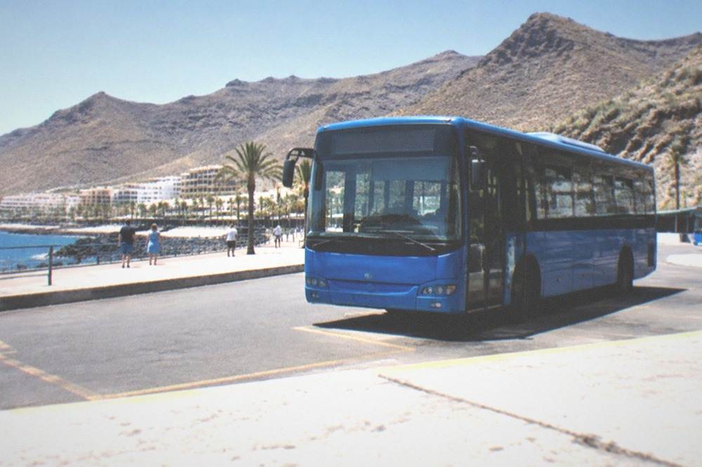 A blue bus at an island bus station with mountains behind