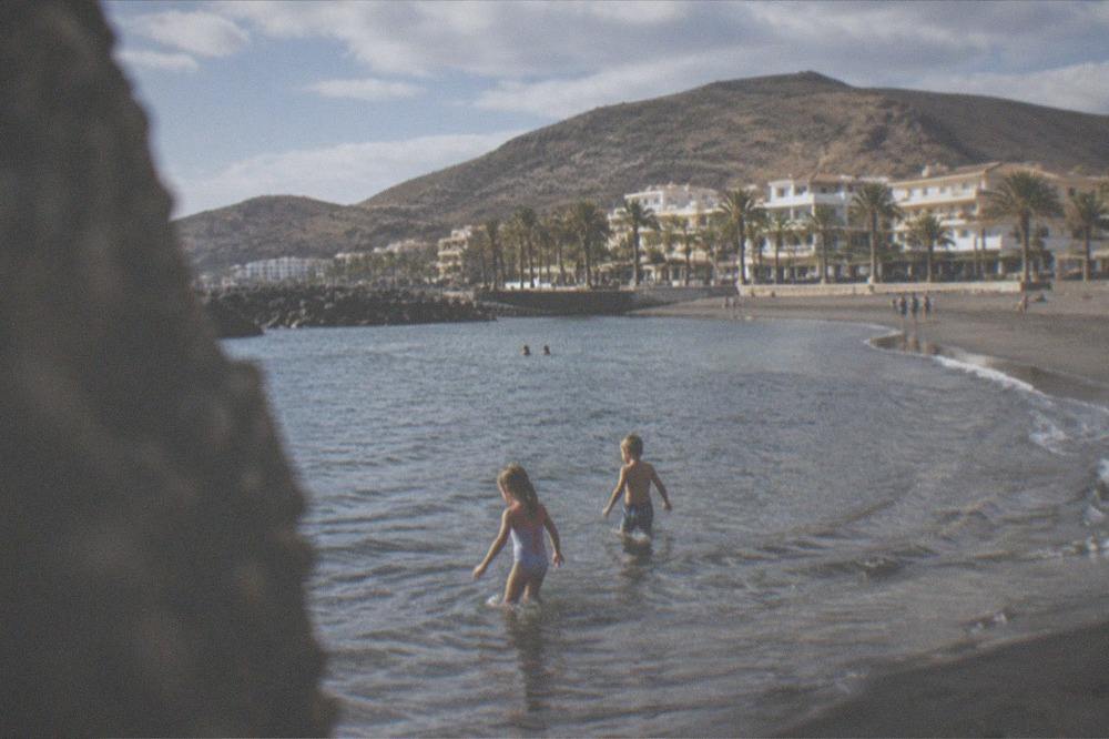 Children playing in shallow clear water at the edge of a sandy beach