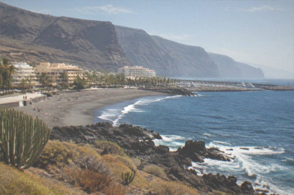 Small resort town beneath tall sea cliffs with a marina and dark sand beach