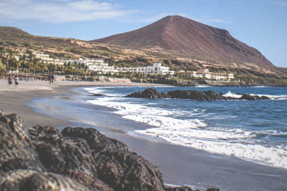 Natural grey sand beach stretching beneath a red volcanic cone