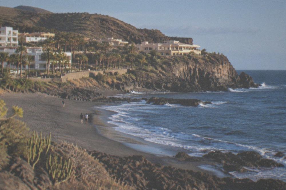 Empty black sand beach beneath green cliffs by the ocean