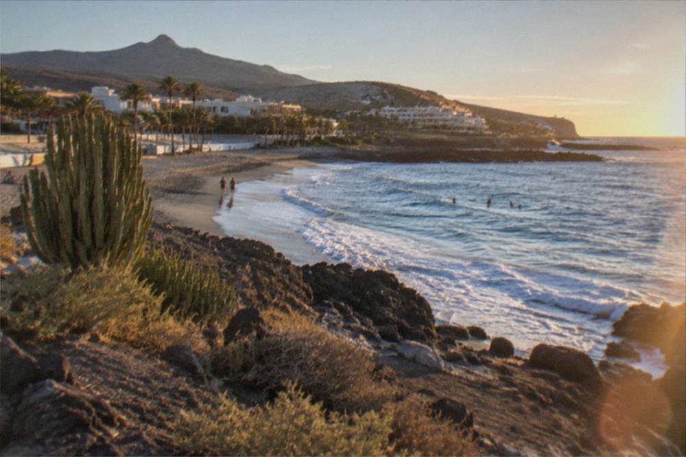 Sunlit beach in autumn with gentle waves and a few swimmers