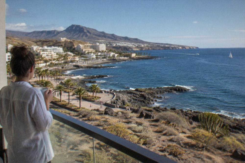 A hotel room balcony with a view over the ocean and a volcanic coastline