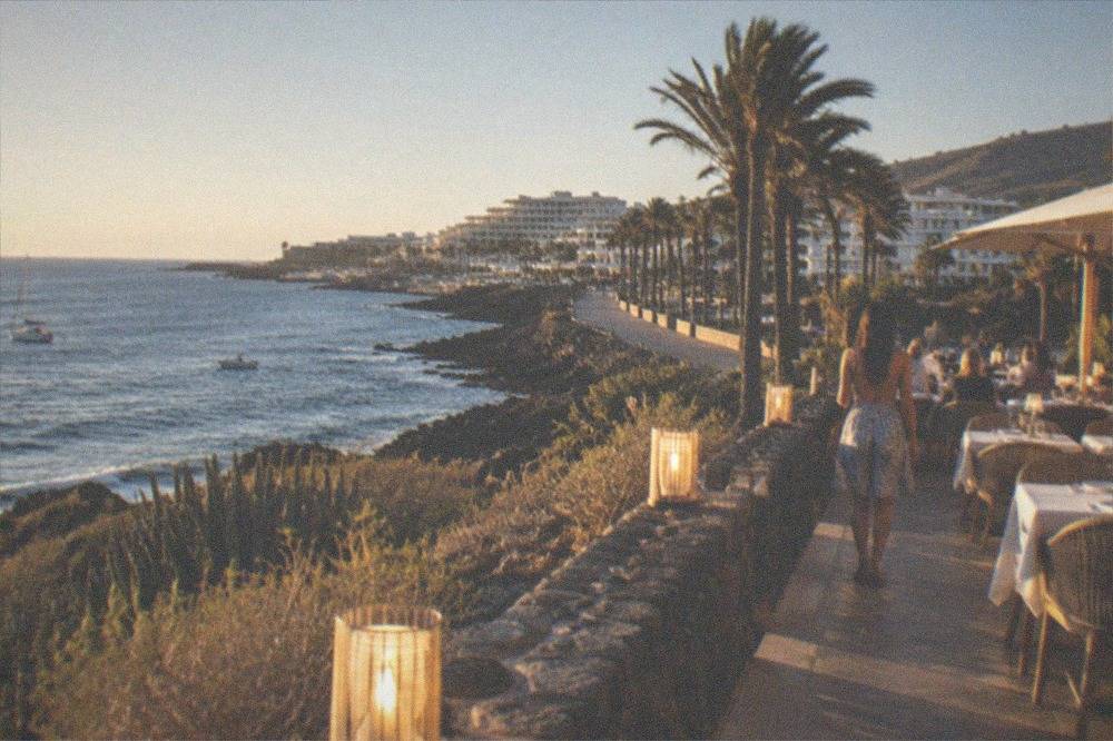 An evening terrace restaurant beside the sea in Costa Adeje with palm trees and lit tables