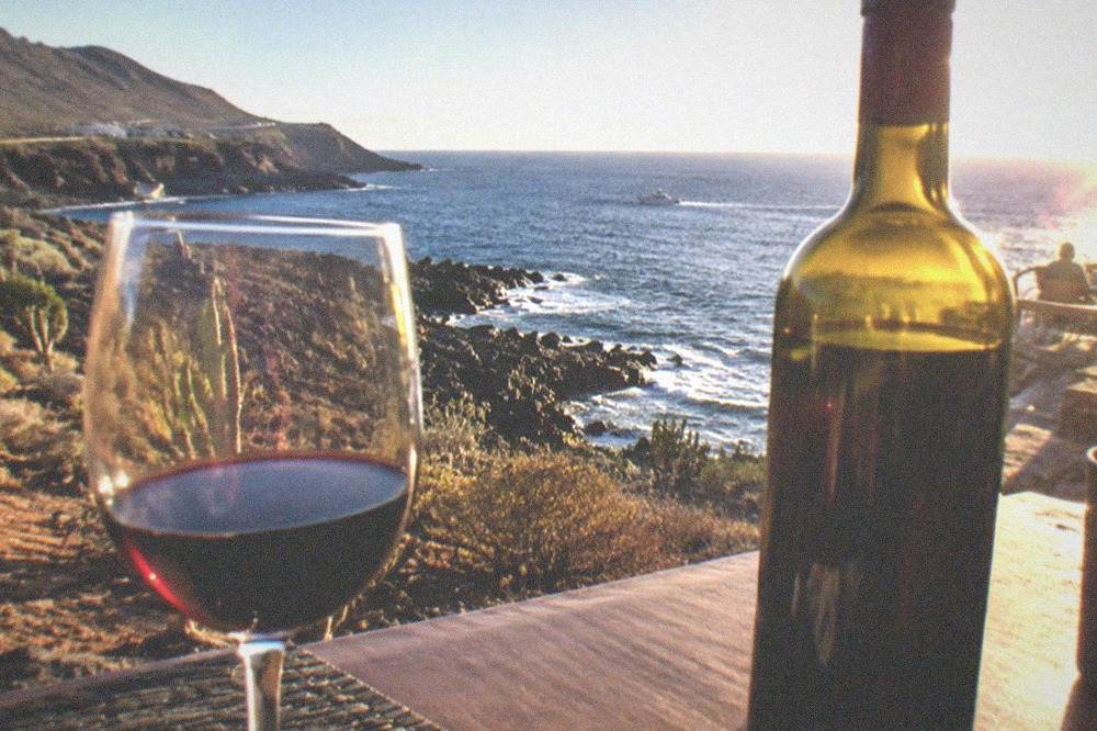 A wine glass and a bottle of Canarian red wine on a restaurant table overlooking the coast