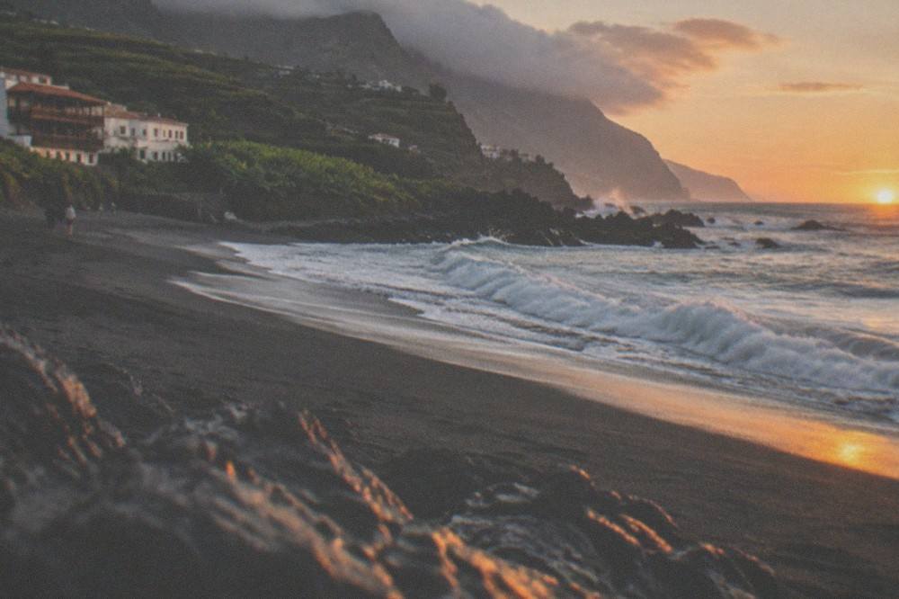 Sunset light over a dark sand beach with waves rolling in