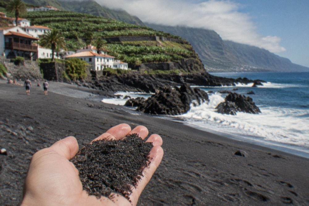 Close view of dark volcanic grains of sand held in a hand