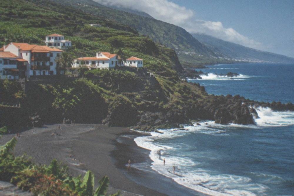 A dark sand cove beneath green cliffs with Atlantic waves
