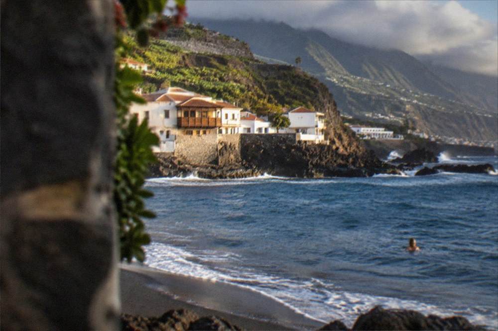 A swimmer in the sea just offshore from a dark sand beach