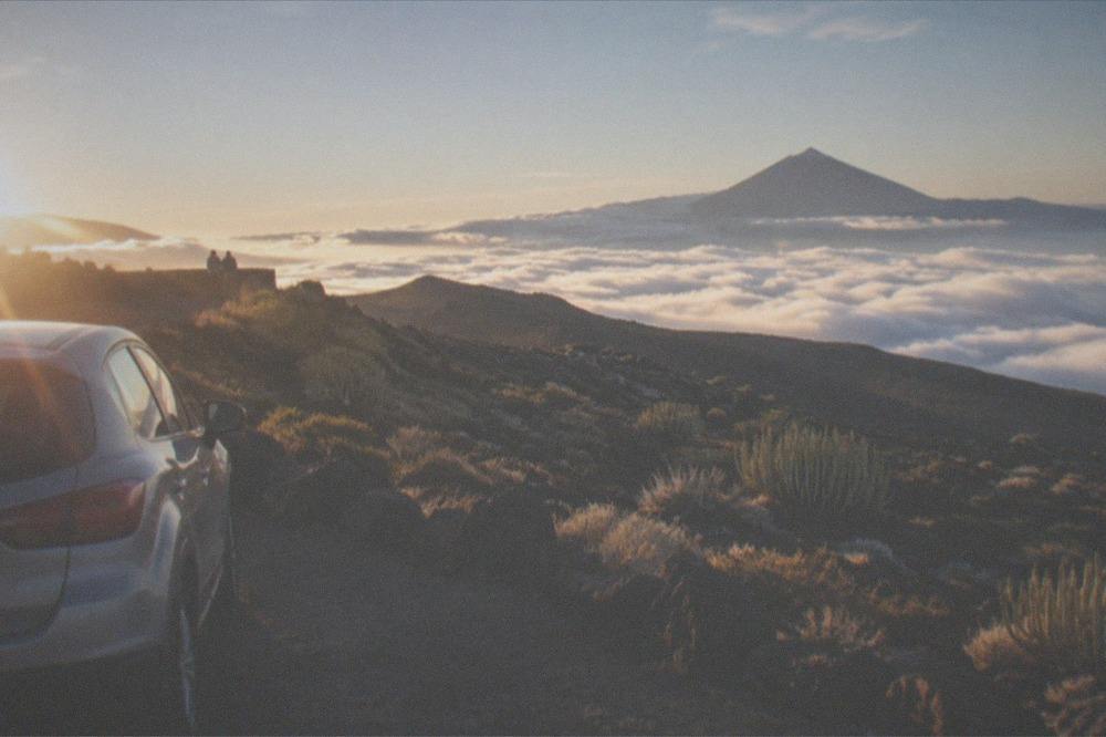 A car parked at a viewpoint above clouds with Mount Teide in the distance