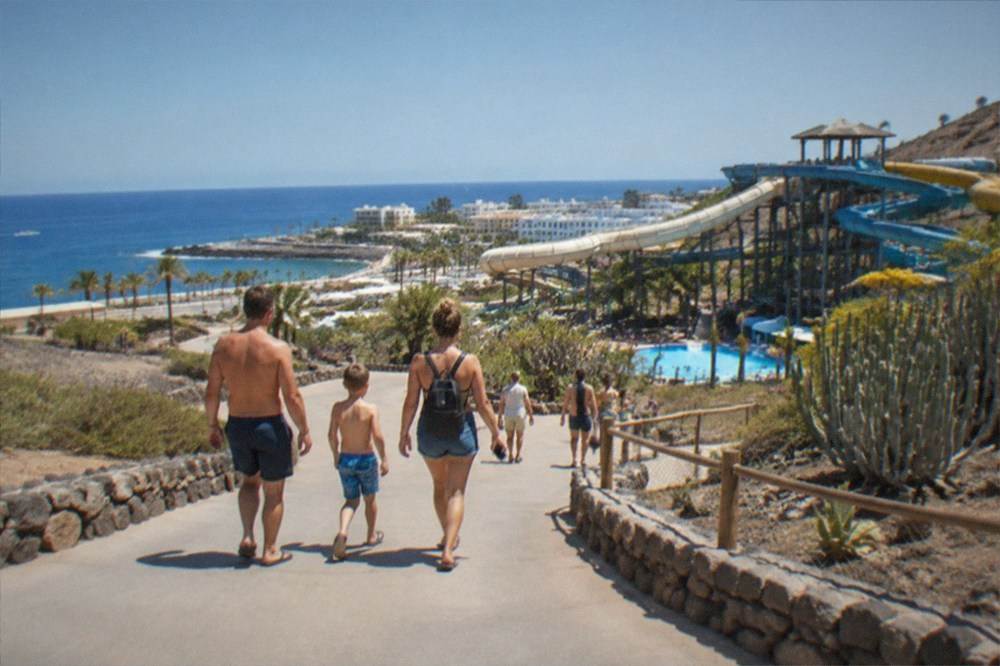 A family walking through a water park carrying a small backpack and a phone