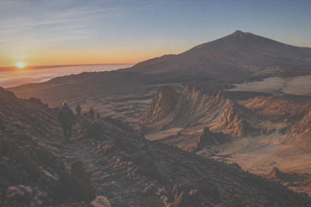 Hikers on a rocky volcanic trail high on Mount Teide at sunrise