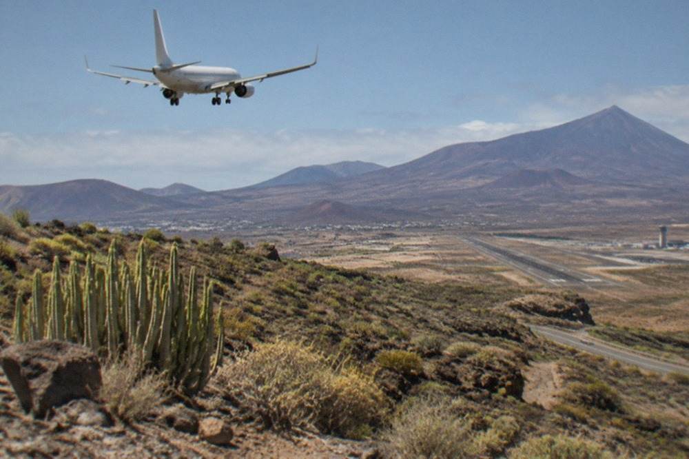 A passenger aircraft on final approach over the Tenerife coastline with volcanic mountains in the distance