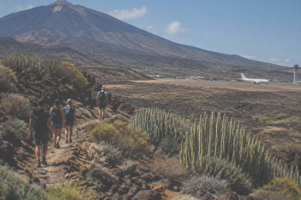 A small group of hikers walking a volcanic trail under a clear blue sky