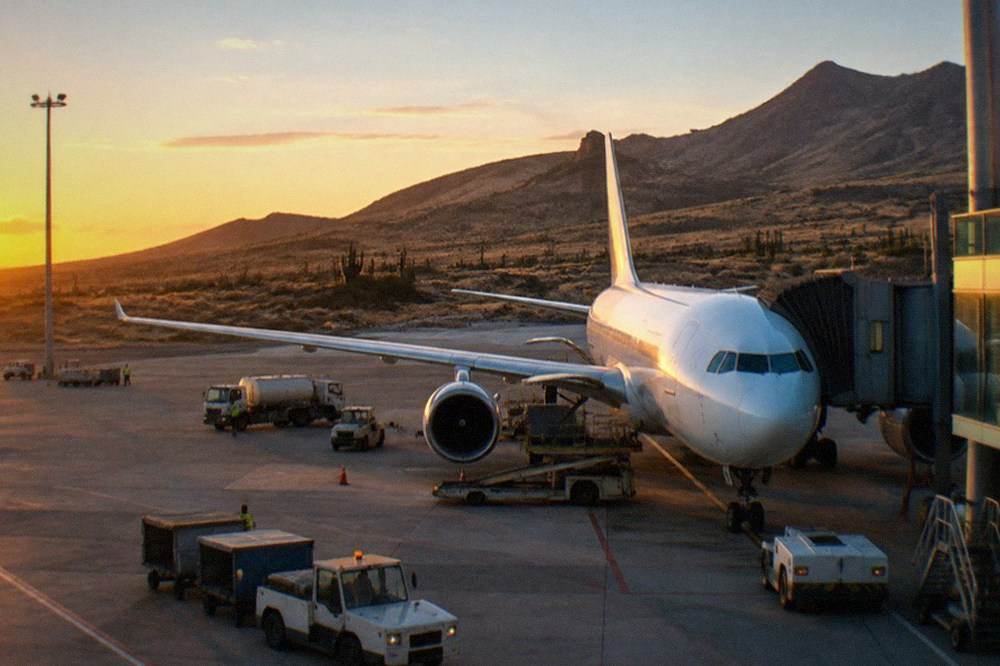 A wide-bodied airliner parked at a terminal gate at dusk with ground vehicles servicing it