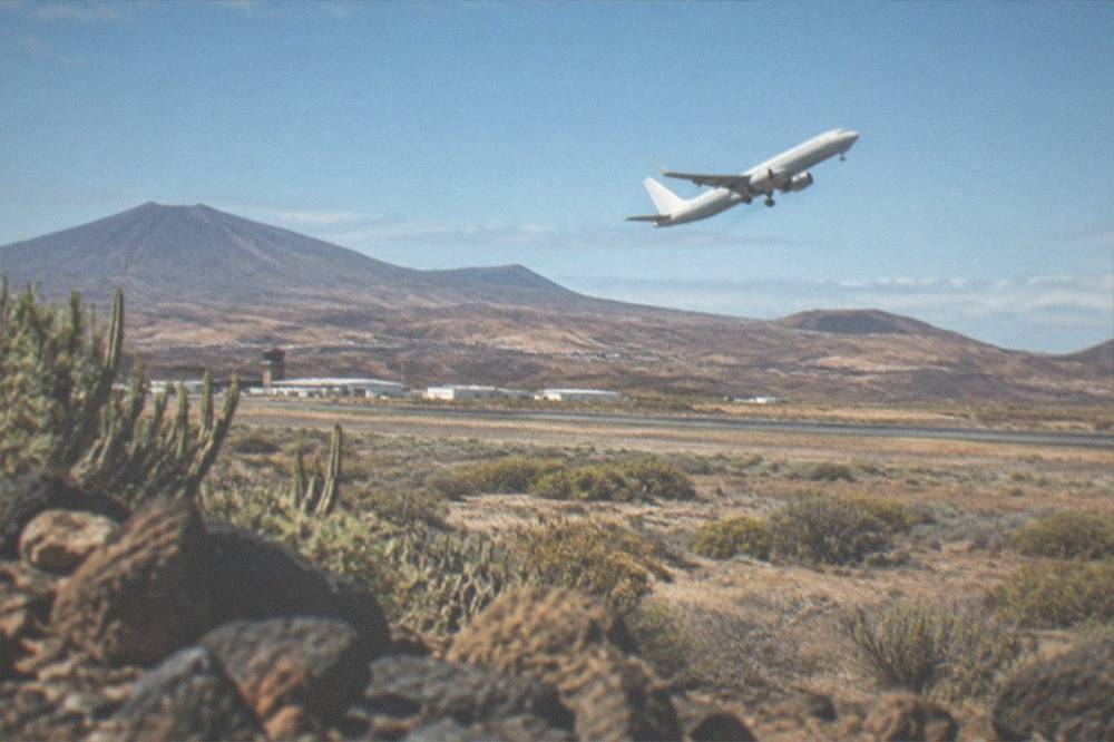 Airliner climbing away from the runway at Tenerife South Airport over a dry inland plain, distant hills behind