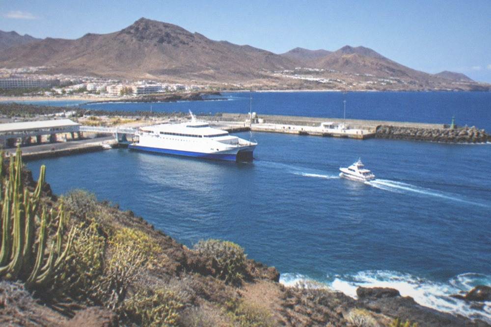 A ferry and a small boat at Los Cristianos harbour with volcanic hills behind