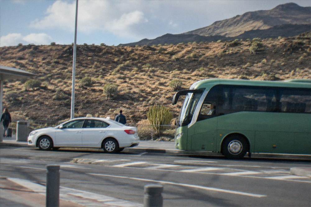 A white taxi and a green intercity bus parked side by side at an airport kerbside