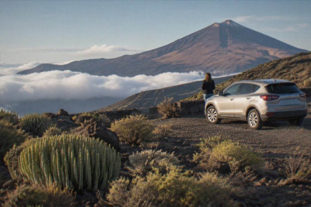 A rental car parked at a mountain viewpoint above clouds with a volcanic cone beyond