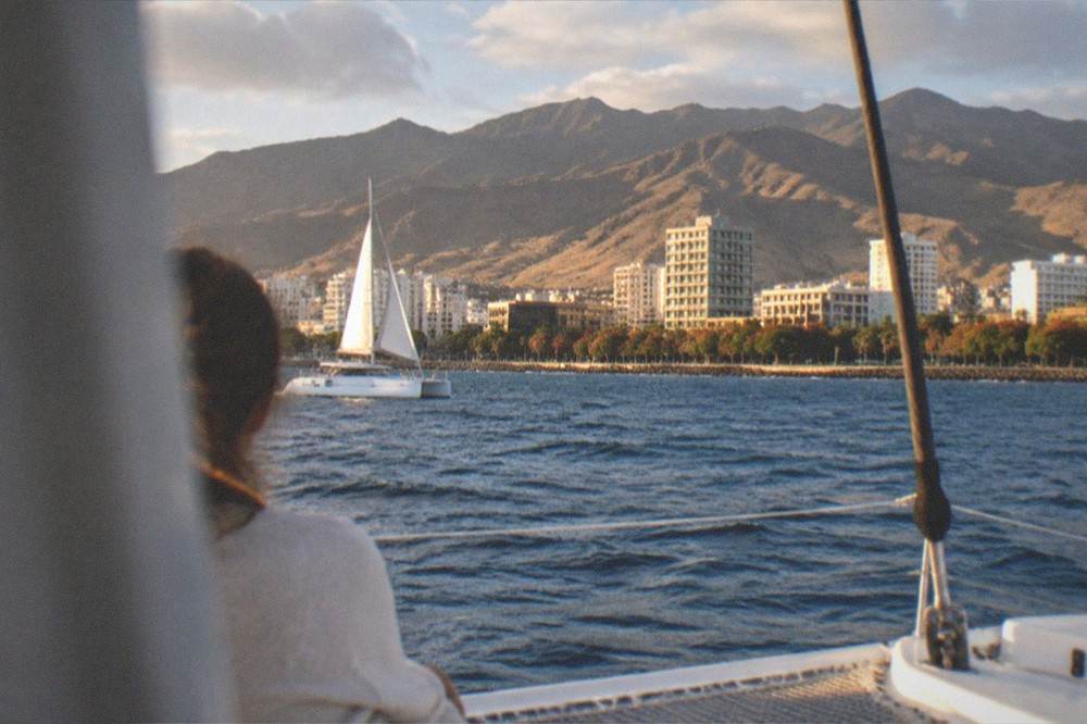 A catamaran sailing along the coast with cliffs in the distance