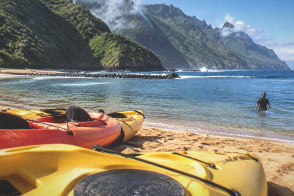 Kayaks on golden sand with a snorkeller entering clear water