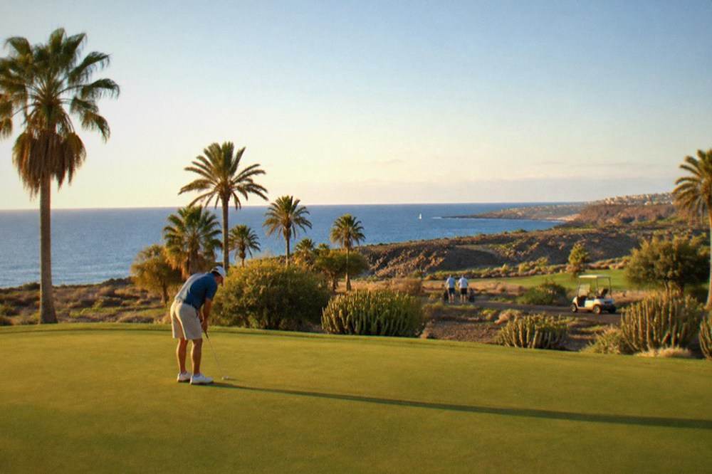 A golfer putting on a green with palm trees and the Atlantic Ocean behind