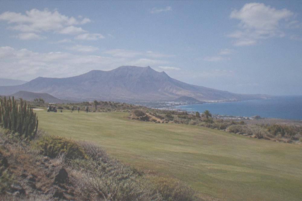 A wide golf fairway with a mountain backdrop under a partly cloudy sky