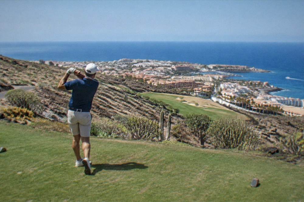 A golfer teeing off with the Atlantic coastline and a resort town visible below