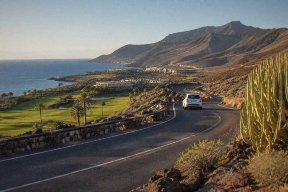 A coastal road winding past a golf resort toward green mountains in Tenerife