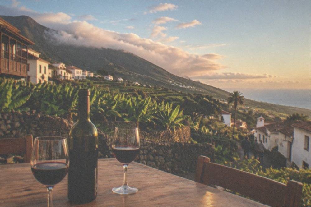 A bottle of house wine and two glasses on a plain wooden tavern table
